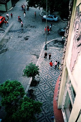 Aerial view of a cobblestone pedestrian zone with geometric tile patterns, flanked by greenery and mid-20th century urban arc...