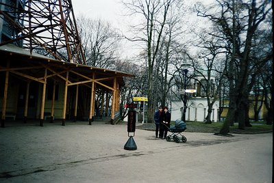 A winter scene in an urban park with Soviet-era architecture. Wooden pavilion with exposed beams and a bus stop shelter in th...