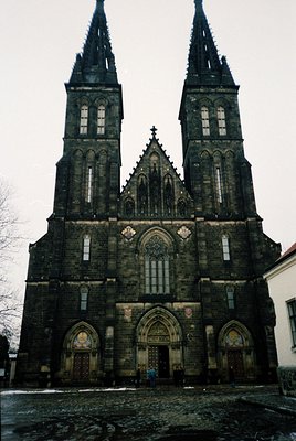 Gothic Revival church façade with twin spires, intricate stone carvings, and pointed arches. Central rose window flanked by t...