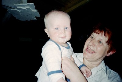 Vintage candid of an adult holding a baby in a dimly lit indoor setting, likely a 1980s-1990s home. Both appear smudged with ...
