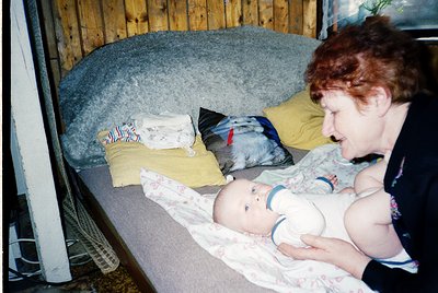 A tender moment captured: a woman breastfeeding an infant in a cozy indoor setting. The scene features a wooden-framed bed wi...