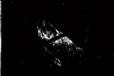 High-contrast black-and-white aerial view of a jagged, irregular coastline with rocky formations and a narrow inlet. Likely a...