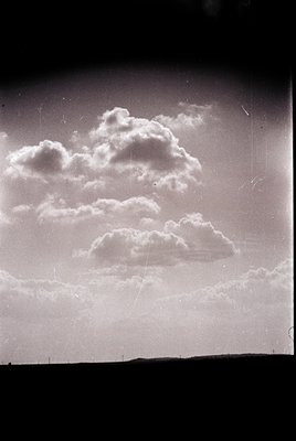 Vintage black-and-white photo of dramatic cumulus clouds with soft, billowing textures against a hazy horizon. Film grain and...