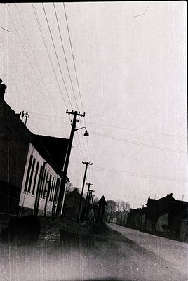Mid-20th century street scene with flooded roadway, likely post-war European town. Two-story brick building with arched windo...