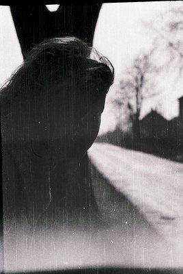 Silhouette of a person leaning against a window frame, rain streaking glass. Urban residential scene with blurred trees and h...