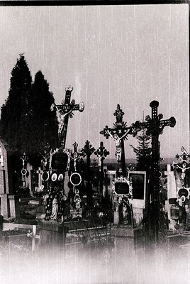 Ornate Orthodox Christian cemetery gravestones with elaborate crosses, wreaths, and portraits, likely Eastern European. Rain-...
