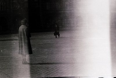 Blurred monochrome street scene with two silhouetted figures walking in opposite directions. Light source creates dynamic, hi...