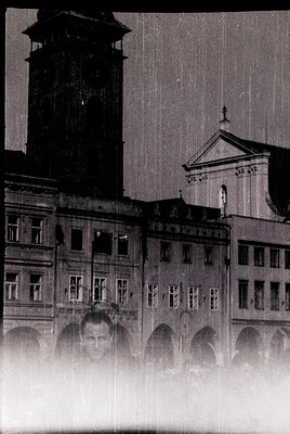 Vintage black-and-white shot of a European urban scene featuring a man in a blurred foreground. Behind him, a row of classica...