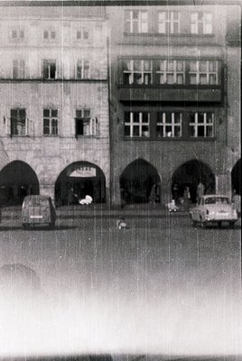 Mid-century European street scene featuring a row of arched ground-floor entrances beneath multi-story residential buildings....
