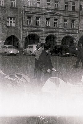 Vintage black-and-white street scene featuring a woman in a patterned coat and hat walking with an umbrella in heavy rain. Mi...