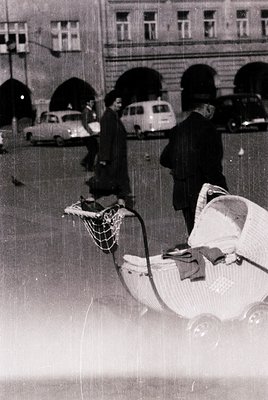 Vintage black-and-white street scene featuring a woman pushing a classic wicker pram with a striped blanket. Mid-20th century...