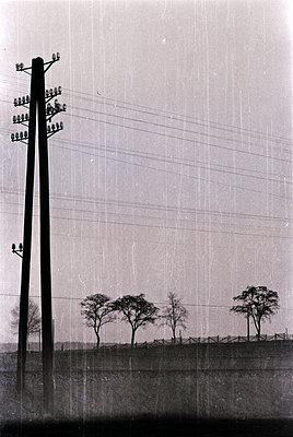 Vintage black-and-white photo of a rural utility pole with multiple crossarms supporting old-style ceramic insulators. A high...