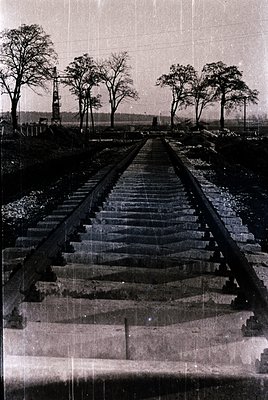 Vintage sepia-toned photograph of a railway bridge with concrete steps and steel railings, spanning a shallow riverbed. Bare ...