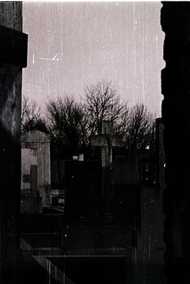 Vintage urban scene viewed through rain-streaked glass, showcasing Brutalist concrete apartment blocks and bare winter trees....