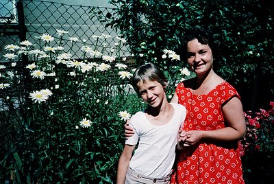 Vintage color portrait of a woman and young girl in a lush garden, likely mid-20th century. The woman wears a floral-patterne...
