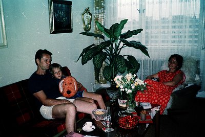 Vintage indoor family portrait from the 1970s, featuring a man, child, and woman in a living room with mid-century decor. The...