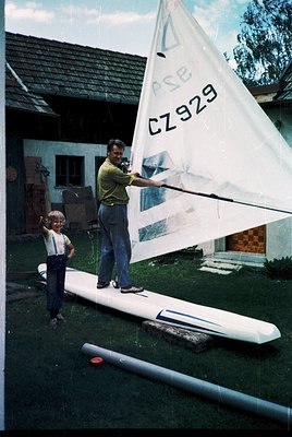A man and child inspect a glider sail marked "CZ929" on a grassy yard, likely 1960s–70s Czechoslovakia. The sail features a t...