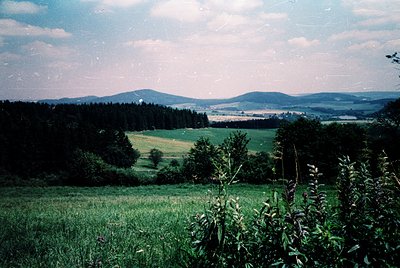 Vintage landscape shot featuring rolling hills, dense forests, and open meadows under a partly clouded sky. The warm sepia to...