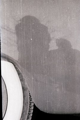 Vintage close-up of a **Kodak Brownie camera** with a blurred silhouette of a person framing the viewfinder. The lens cap is ...