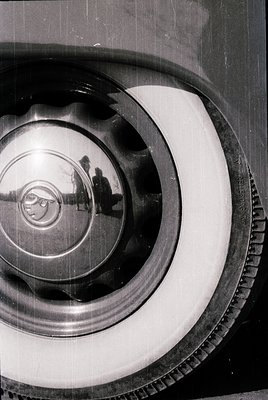 Vintage close-up of a polished chrome car hubcap reflecting a blurred silhouette of a person in motion. Circular design with ...
