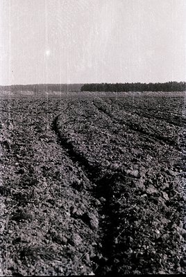 Aerial view of plowed agricultural field with deep furrows, likely post-harvest or pre-planting. The horizon shows a distant ...