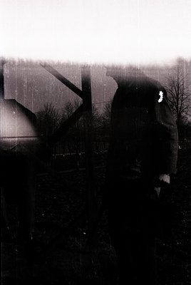 Vintage sepia-toned photograph of a lone figure silhouetted against a dimly lit industrial landscape. The person stands near ...