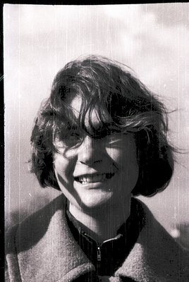 Vintage black-and-white portrait of a young woman with short, voluminous hair and a warm smile. She wears a collared jacket w...