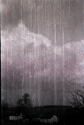 Intense rainstorm captures heavy vertical downpours over a flat landscape, with sparse trees and distant structures. Black-an...