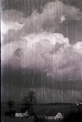 Classic black-and-white depiction of a heavy rainstorm over a rural landscape. Dense rain curtains obscure visibility, with d...