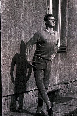 Young man in mid-stride on a brick staircase, leaning casually with one hand on the railing. Wearing a short-sleeve sweater a...