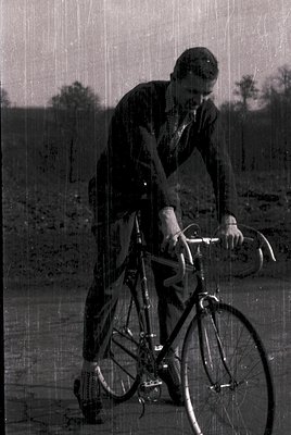 Mid-century vintage cyclist in rural setting, wearing layered clothing and a cap. Classic road bike with drop handlebars and ...
