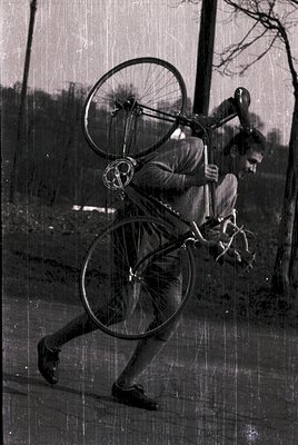 Vintage black-and-white photo of a man mid-fall with a large-wheeled bicycle, likely a 1920s–1940s design. Urban or suburban ...