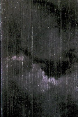 Rain streaks on a dark, vertical-textured surface—likely glass or a wet window—capturing motion blur from heavy precipitation...