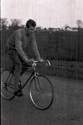 Man in vintage cycling gear rides a classic road bike on a rural road, mid-1970s. Lightweight frame, drop handlebars, and hig...