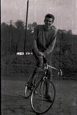 Vintage black-and-white photo of a young man in a sweater and trousers posing on a classic road bike, likely mid-20th century...
