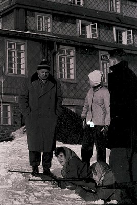 Black-and-white snapshot of three adults and a child in winter attire, likely Eastern Europe, 1950s–1960s. Snow-covered court...