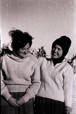 Two women in matching 1960s-style knitwear pose outdoors, likely in a rural or suburban setting. The woman on the left wears ...