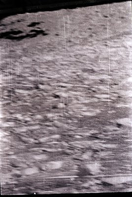 Grainy black-and-white aerial photo of lunar surface with prominent craters and rugged terrain. Scratch marks and exposure fl...