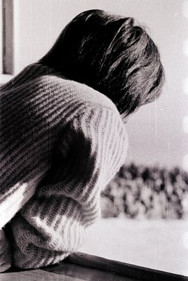 Black-and-white portrait of a child leaning against a window sill, peering out. The child wears a striped sweater and has sho...