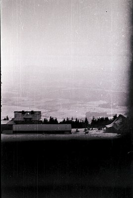Vintage black-and-white aerial view of a mid-20th-century industrial complex with angular concrete structures and a low-lying...