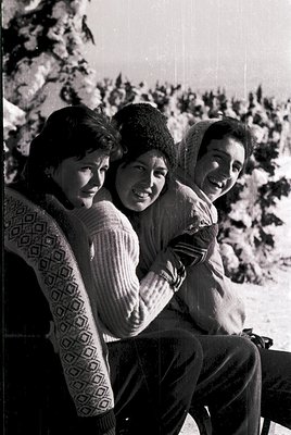 Three individuals pose together in a snowy alpine setting, mid-20th century. Left wears a patterned sweater; center, a knitte...