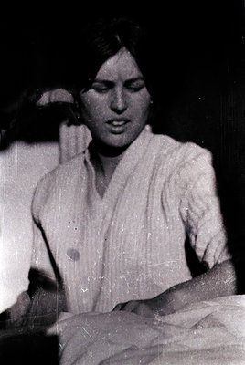 Vintage black-and-white portrait of a woman in a loose, high-necked blouse, seated indoors with a blurred background. Her exp...