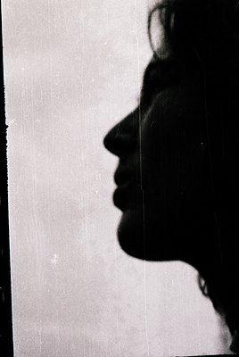 Silhouette of a person facing a light source, likely a window or door, with visible hair and partial collar. Monochrome, high...