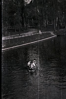 Vintage black-and-white photo of a serene lakeside scene with three figures in a small wooden boat. A lone person stands on a...