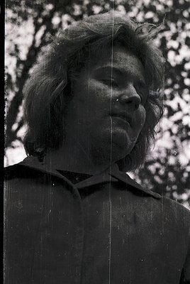 Portrait of a person with short, voluminous hair and a relaxed expression, captured in black-and-white. The blurred backgroun...