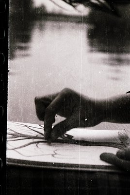 Vintage black-and-white photo of a person writing at a desk, likely mid-20th century. The blurred background suggests a focus...