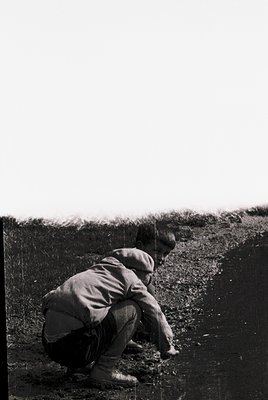 Black-and-white photo of two individuals kneeling in a trench, likely during construction or excavation. The scene suggests m...