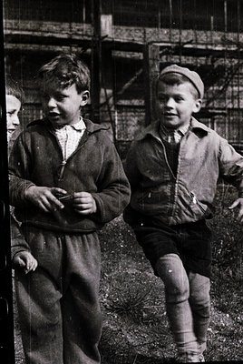Mid-20th century boys in vintage sportswear—one in a knit cap, both in knee-high socks and long pants—pose outdoors near rust...