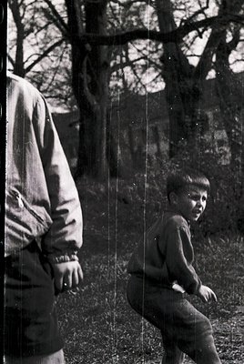 Black-and-white candid of an adult and child in a wooded area, likely mid-20th century. The adult wears a long-sleeve shirt a...
