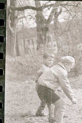 Vintage black-and-white photo of an adult and child playing in a wooded area, likely mid-20th century. The adult, wearing a c...